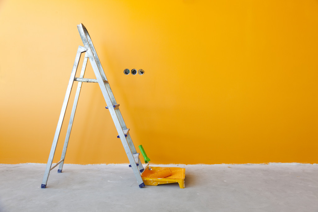 A ladder and roller paint in front of a yellow wall