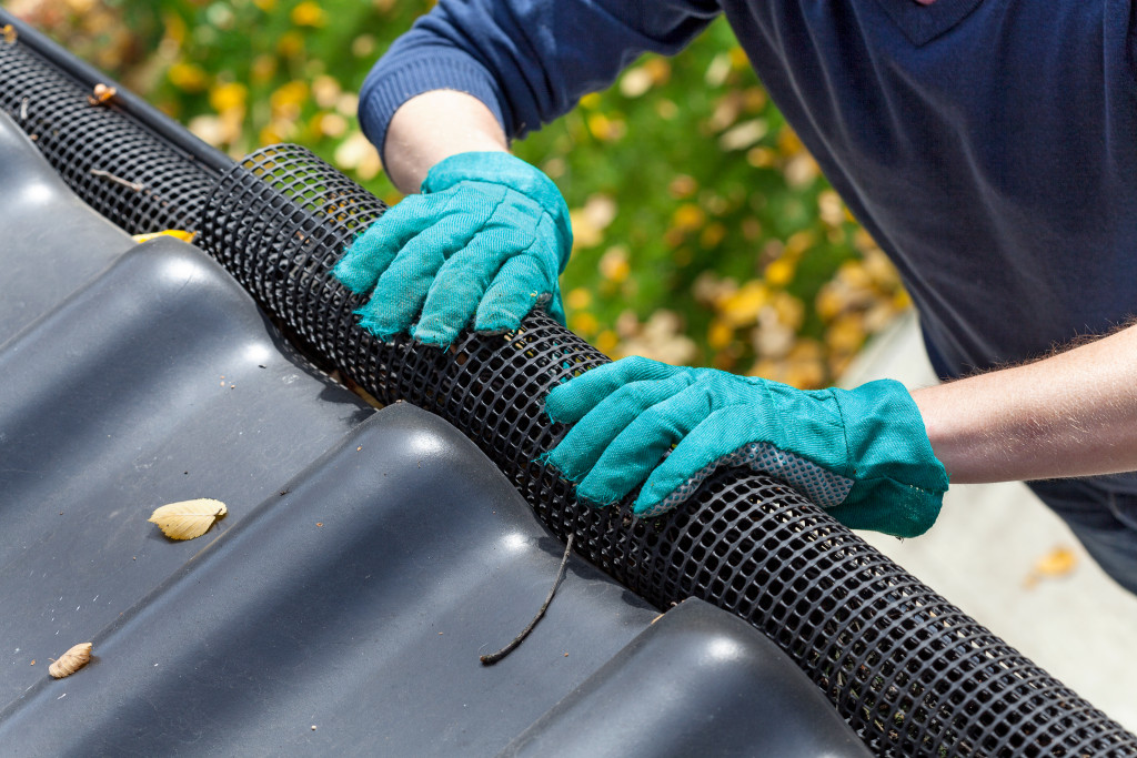 man's hands in gloves securing gutters with black net