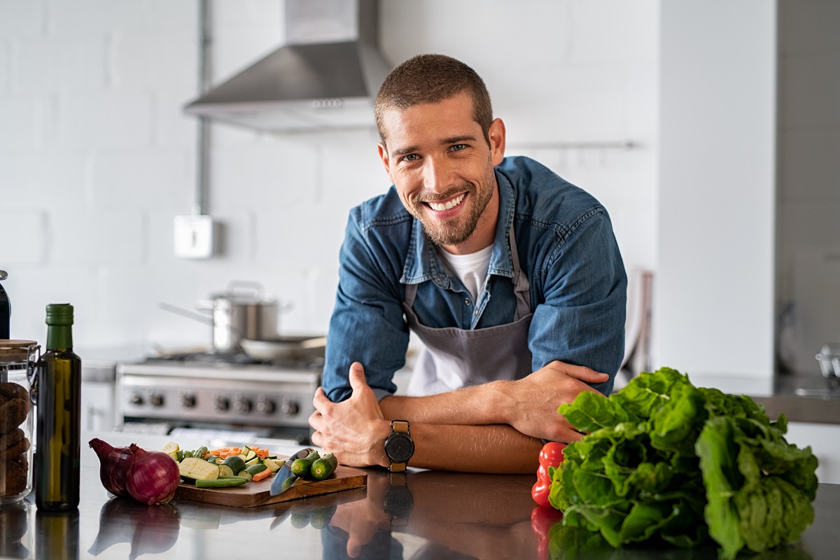 Portrait of happy casual guy in apron leaning on steel counter